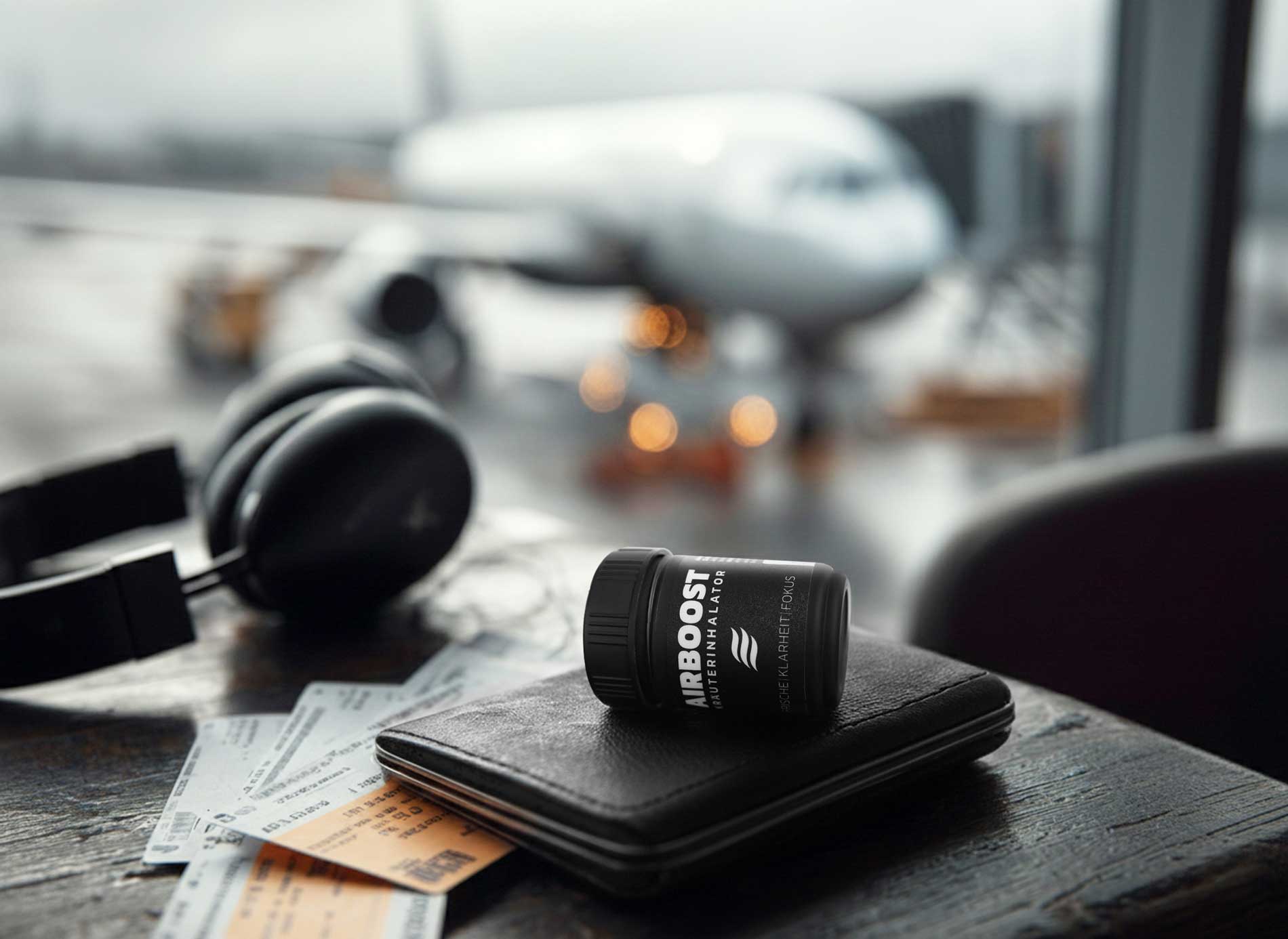 AIRBOOST Kräuterinhalator im Alltag auf einer Geldbörse am Flughafen mit einem Flugzeug im Hintergrund - perfekt zum Reisen und für Business Reisen für sofort freien Atem